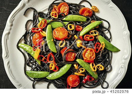 fresh delicious black vegan spaghetti with tomatoes, chili pepper, on a white plate fresh delicious black vegan spaghetti with tomatoes, chili pepper, on a white plate 45202076