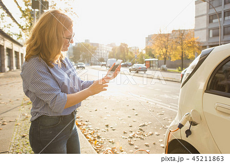 Young woman is standing near the electric car Young woman is standing near the electric car 45211863