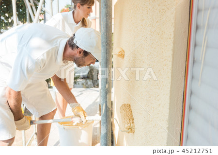 Painter and colleague painting wall with roller 45212751