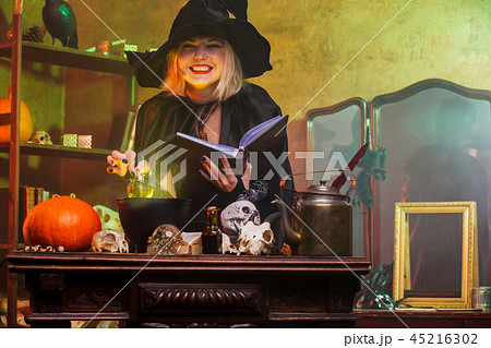 Portrait of smiling witch in black hat reading spell over pot with green steam Portrait of smiling witch in black hat reading spell over pot with green steam 45216302