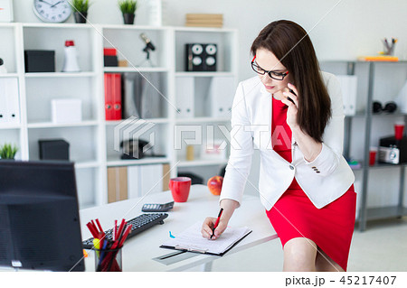 A young girl sat down on a Desk in the office and holding a phone. A young girl sat down on a Desk in the office and holding a phone. 45217407