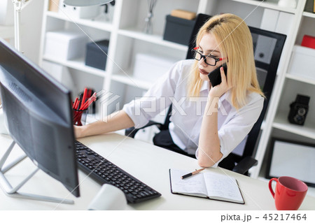 A young girl working at a computer in the office and talking on the phone. A young girl working at a computer in the office and talking on the phone. 45217464