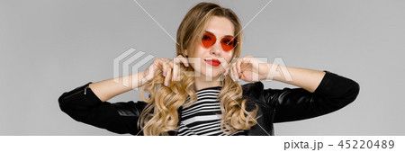 A beautiful girl in red glasses holds her blond hair with her hands A beautiful girl in red glasses holds her blond hair with her hands 45220489