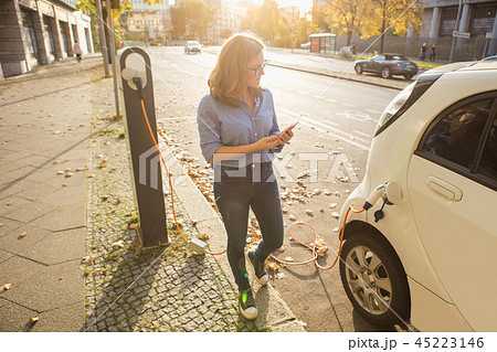 Young woman is standing near the electric car  45223146