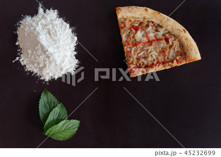 Slice of pizza, flour and leaves on black ground Slice of pizza, flour and leaves on black ground 45232699