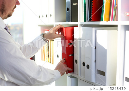 Male arms pick red file folder from office book shelf Male arms pick red file folder from office book shelf 45243439