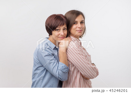 Beautiful maturesenior mom and her adult daughter are hugging, looking at camera and smiling. Beautiful maturesenior mom and her adult daughter are hugging, looking at camera and smiling. 45246201