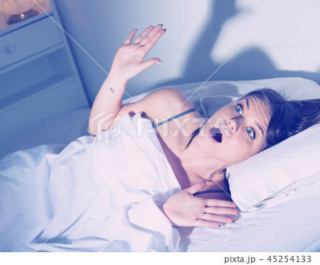 Young female is worried on bed, because oversleep in bedroom Young female is worried on bed, because oversleep in bedroom 45254133