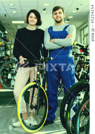 Young woman and seller standing with bicycle in the store indoor Young woman and seller standing with bicycle in the store indoor 45254254