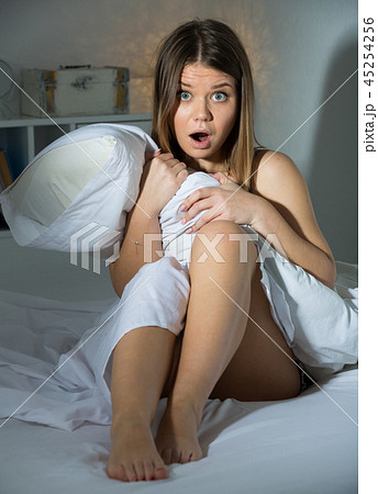 Worried young woman is oversleep, sitting on bed in bedroom Worried young woman is oversleep, sitting on bed in bedroom 45254256