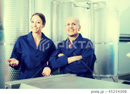 Portrait of smiling two coworkers standing on wine factory Portrait of smiling two coworkers standing on wine factory 45254306
