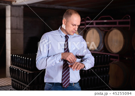 Confident male winemaker degusting red wine in wine cellar near bottles racks Confident male winemaker degusting red wine in wine cellar near bottles racks 45255094