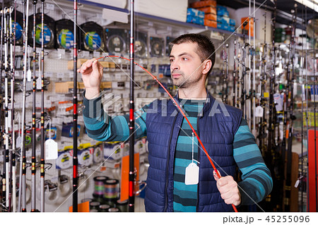 serious male choosing fishing rod for fishing in the sports shop serious male choosing fishing rod for fishing in the sports shop 45255096