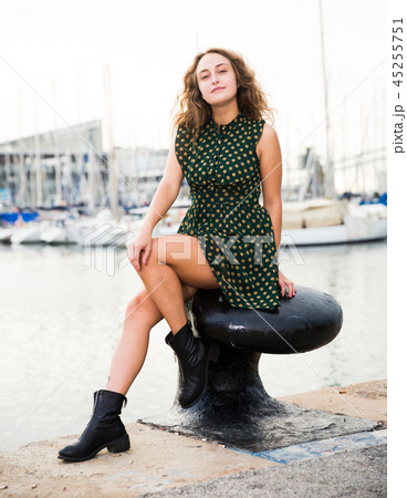 Young attractive woman tourist sitting at stone in port with sailboats 45255751