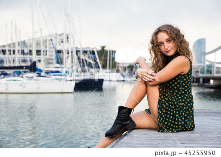 Young attractive woman tourist sitting at quay with sailboats on background 45255950