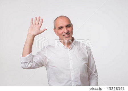Handsome attractive european man waiving hand in hello gesture while smiling cheerfully. 45258361
