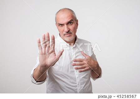 Mature man in yellow shirt showing sign stop with hand. 45258567