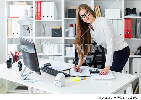 A young girl stands bent over near the table and works with a computer, documents and calculator A young girl stands bent over near the table and works with a computer, documents and calculator 45275298