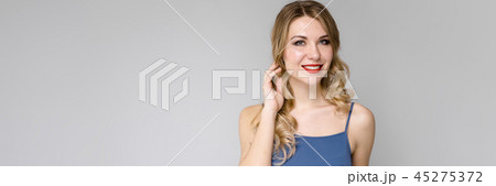 Charming girl with white long curly hair. Girl in a blue top and blue pants on gray background 45275372