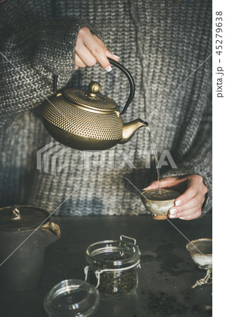 Female in sweater pouring green tea from pot into cup Female in sweater pouring green tea from pot into cup 45279638