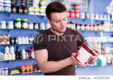Young muscular man choosing sport nutrition products in shop Young muscular man choosing sport nutrition products in shop 45285201