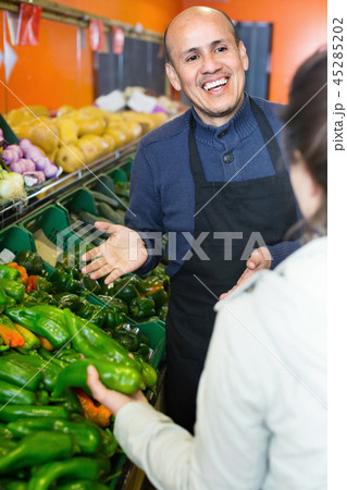 Young woman buying seasonal vegetables in grocery from mature seller 45285202