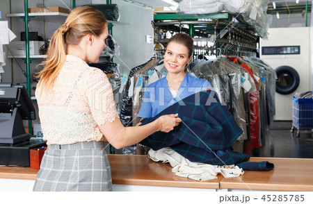 Young woman worker of laundry taking clothes for dry cleaning from female client 45285785