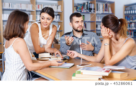 Happy young university students preparing for exam together, brainstorming in library Happy young university students preparing for exam together, brainstorming in library 45286061