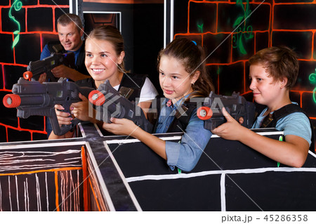 Smiling boy and girls aiming laser guns and playing laser tag game with parents 45286358