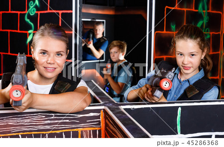Modern young woman and teen girl with laser pistols playing laser tag in dark labyrinth 45286368