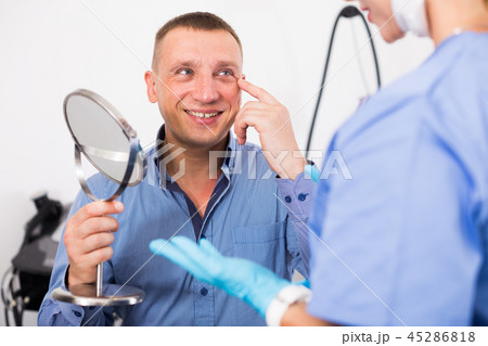 Female specialist is analysing skin of patient with using mirror before the procedure Female specialist is analysing skin of patient with using mirror before the procedure 45286818