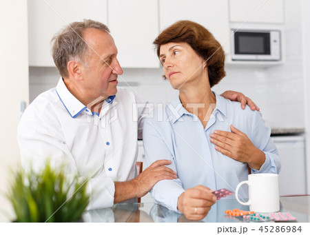 Unhappy mature couple sittimg at kitchen table and taking drugs in home 45286984