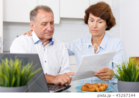 Mature man and woman with documents talking while working at laptop 45287144