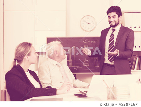 Office manager male is reading financial report to colleagues on meeting Office manager male is reading financial report to colleagues on meeting 45287167