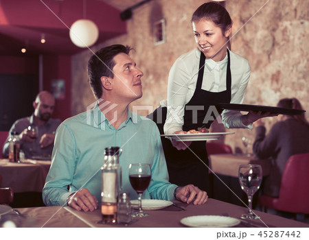 Positive waitress bringing delicious meal to young man Positive waitress bringing delicious meal to young man 45287442