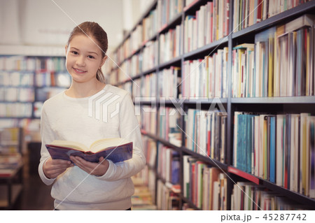 Intelligent preteen girl standing alone near bookcase in library Intelligent preteen girl standing alone near bookcase in library 45287742