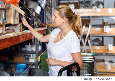 Young woman choosing construction materials at shelves in modern building shop Young woman choosing construction materials at shelves in modern building shop 45287827
