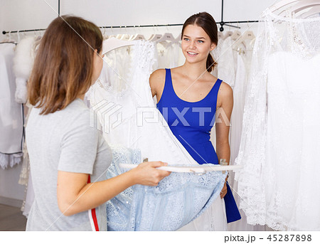Girl choosing white dress with help of assistant Girl choosing white dress with help of assistant 45287898