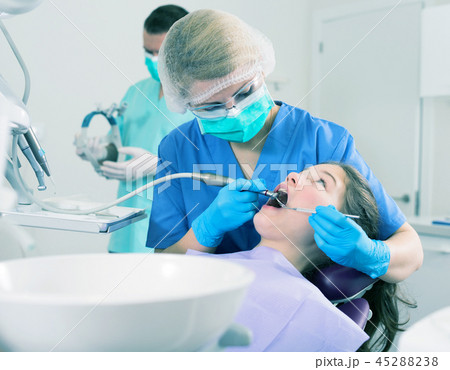 Female dentist treating girl patient with male assistant Female dentist treating girl patient with male assistant 45288238