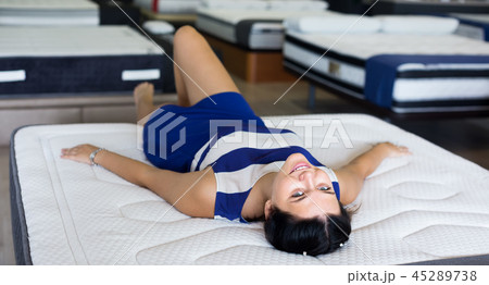 smiling customer girl is lying testing new mattress before buying it in shop smiling customer girl is lying testing new mattress before buying it in shop 45289738