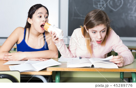 Two girls are eating sandwich at the desk and writing homework Two girls are eating sandwich at the desk and writing homework 45289776