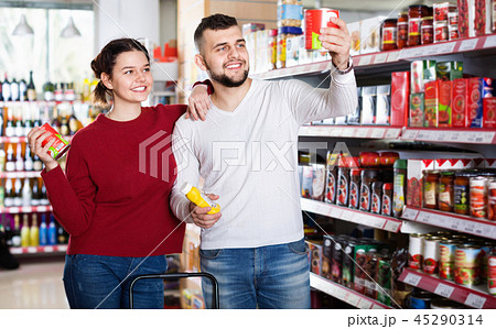 Couple standing near shelves with canned goods at store 45290314