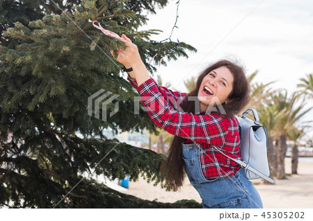 People, holidays and celebrations concept - young woman decorating christmas tree outdoors 45305202