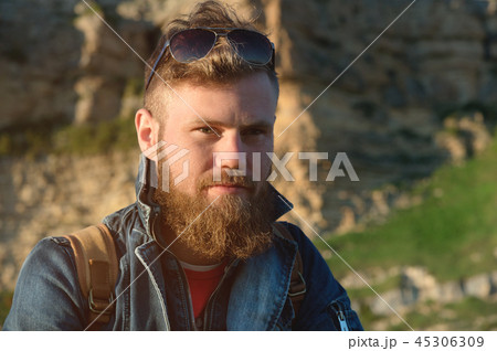 Close-up portrait of a bearded stylish traveler in a cap against epic rocks. Time to travel concept 45306309