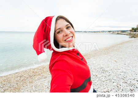 Christmas, humor and people concept - young woman in Santa suit making selfie near the sea at summer Christmas, humor and people concept - young woman in Santa suit making selfie near the sea at summer 45306540
