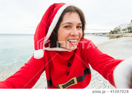 Christmas, humor and people concept - young woman in Santa suit making selfie near the sea at summer Christmas, humor and people concept - young woman in Santa suit making selfie near the sea at summer 45307028
