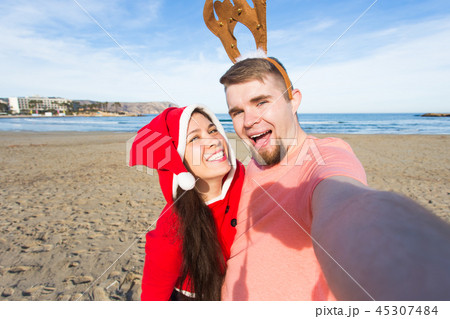 Christmas, humor, people concept - Happy Christmas couple having fun taking selfie on beach 45307484