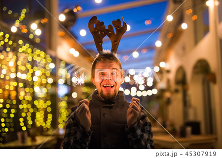 People, holidays and christmas concept - surprised man in deer's horns holding two bengals light or 45307919