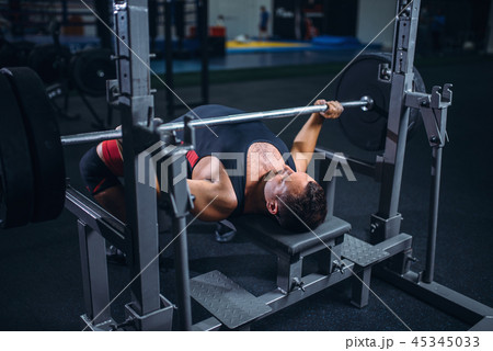 Weight lifter on exercise machine with barbell 45345033