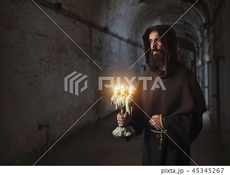 Medieval monk in robe holds a candlestick in hands 45345267